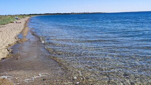 Une plage propre avec une eau calme, un rivage sablonneux et une côte visible au loin.