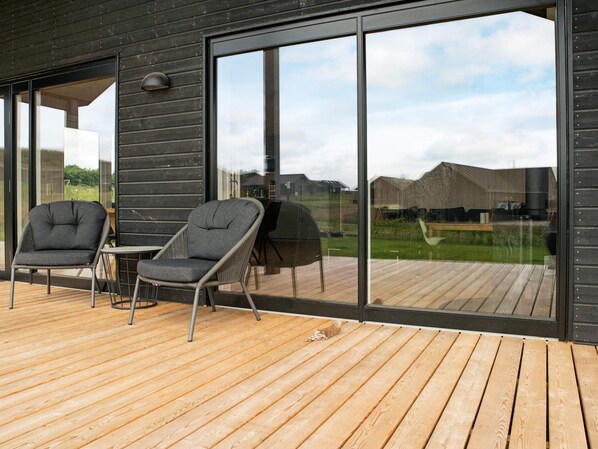 A modern outdoor deck with two chairs and a table, large sliding glass doors, and a view of a residential area.