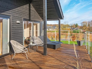 A modern outdoor deck with wooden flooring, two wicker chairs, a small table, and a black outdoor sofa. - 10 Person Holiday Home in Haderslev-by Traum (Haderslev)