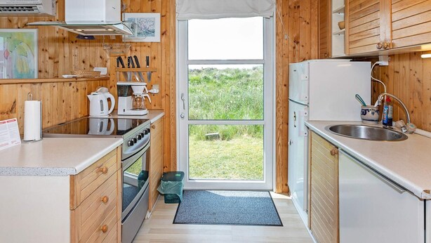 Cocina compacta con armarios de madera, cafetera, lavamanos y vistas al exterior.