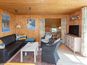 A cozy room with a wooden ceiling, a sofa, a wicker chair, a TV, and a cabinet.