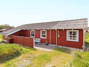 Ett rött trähus med ett sluttande tak, en bänk utanför och en skylt med nummer 12 på dörren.