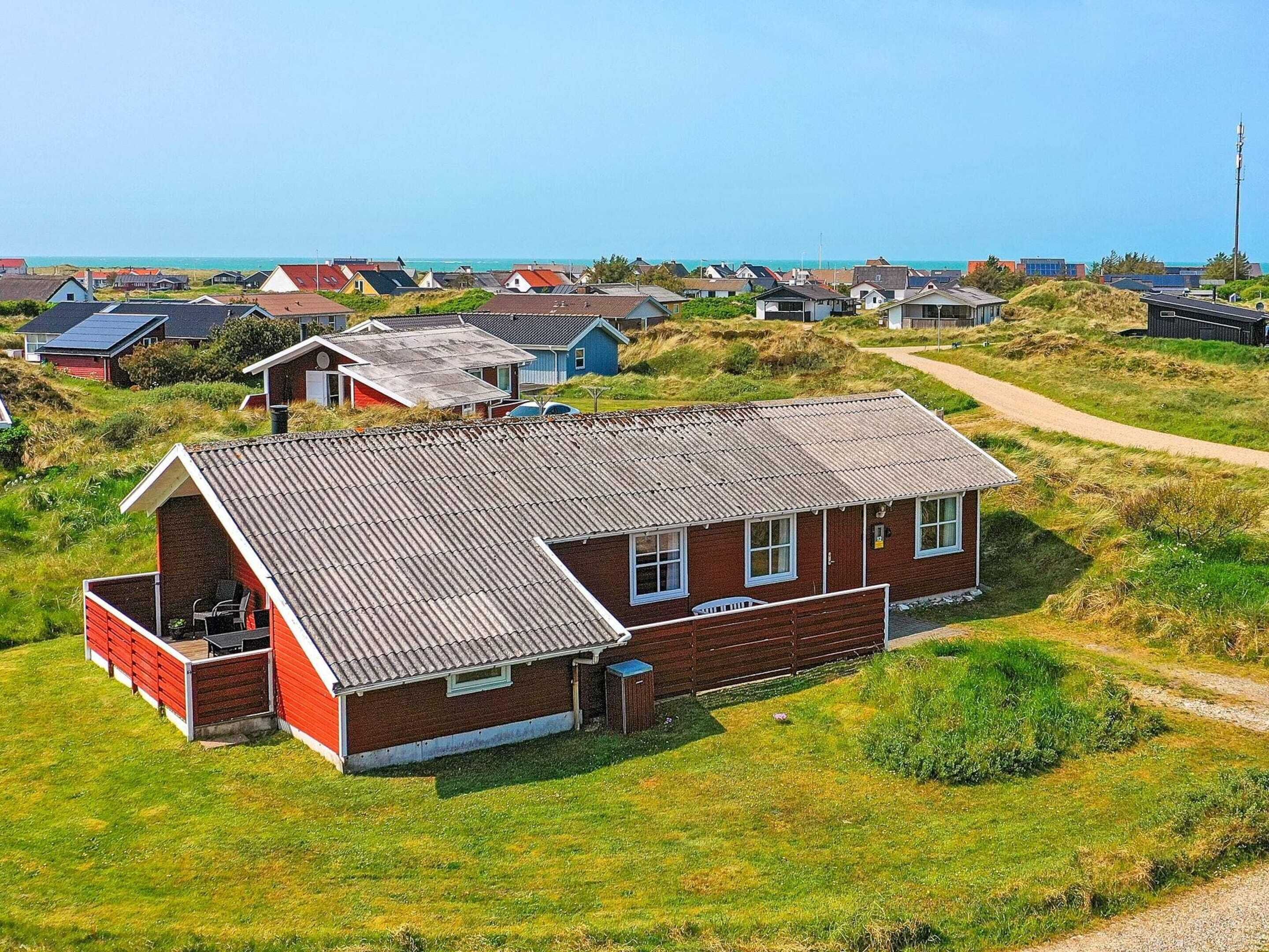 A red brick house with a sloped roof, a small attached shed, and a pathway leading to the sea.
