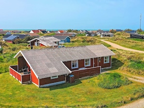 Een rode bakstenen woning met een schuin dak, een klein bijgebouw en een pad dat naar de zee leidt.