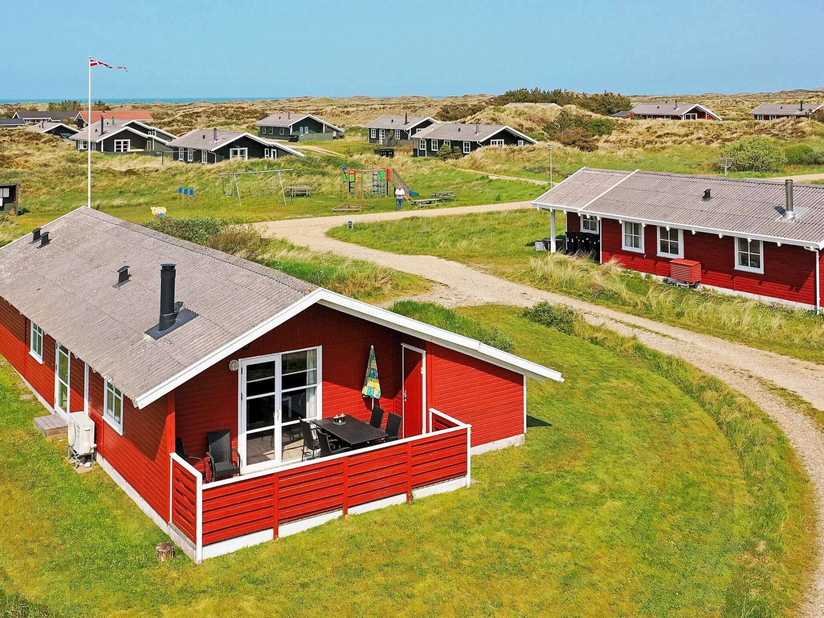 A red cabin with a porch and a view of a dune landscape.
