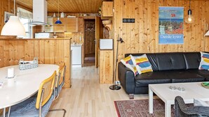 Interior acogedor de una cabaña con comedor, sofá de cuero negro y un cartel en la pared.