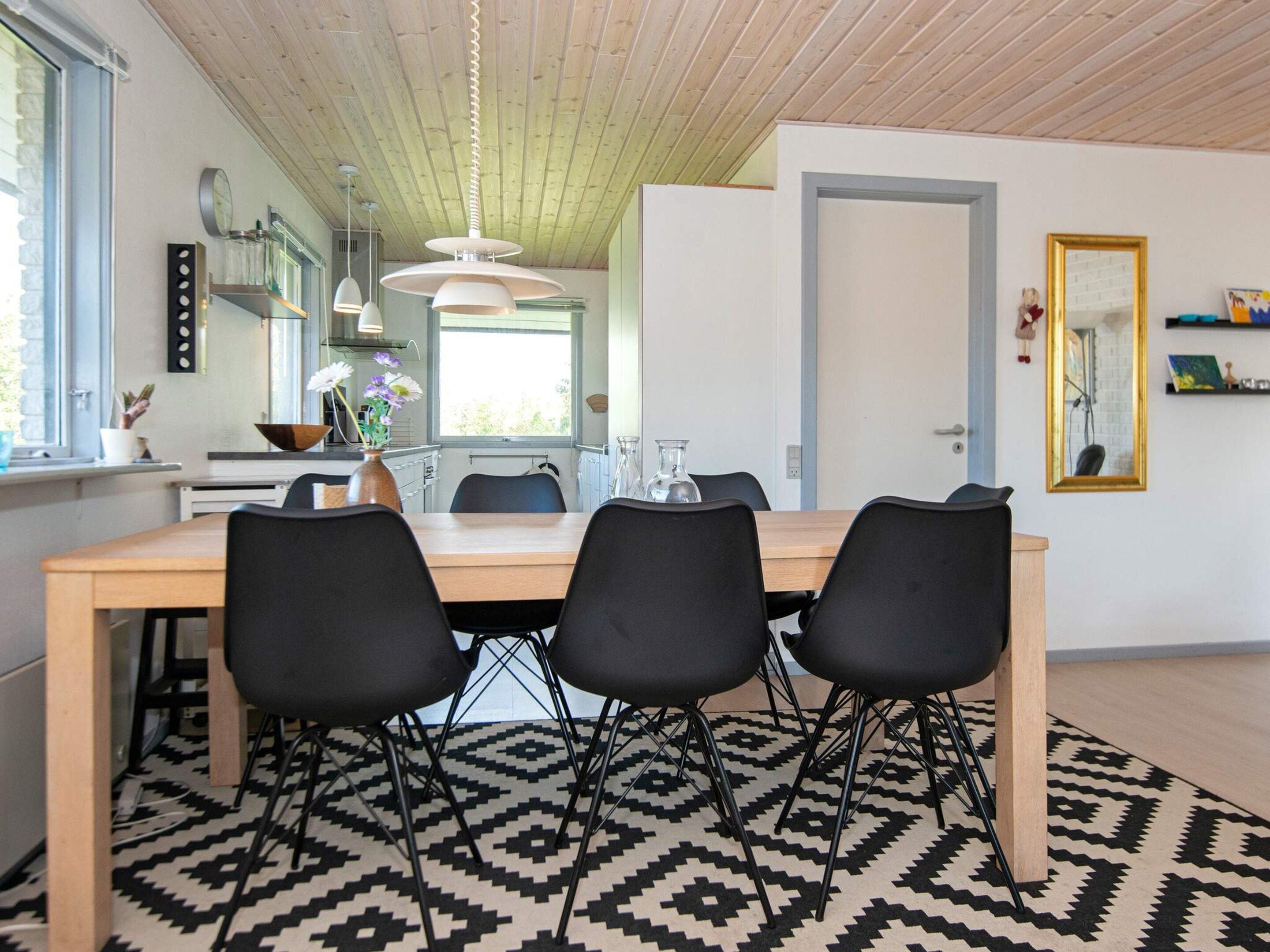 Un coin repas avec une table en bois, des chaises noires et un tapis à motifs.
