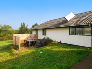 Een huis met een gevel van witte bakstenen, een schuin dak en een omheinde achtertuin met een tafel en stoelen.