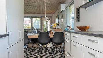 Une cuisine moderne avec des meubles blancs, un coin repas agrémenté d’un tapis à motifs et une vue sur l’extérieur.