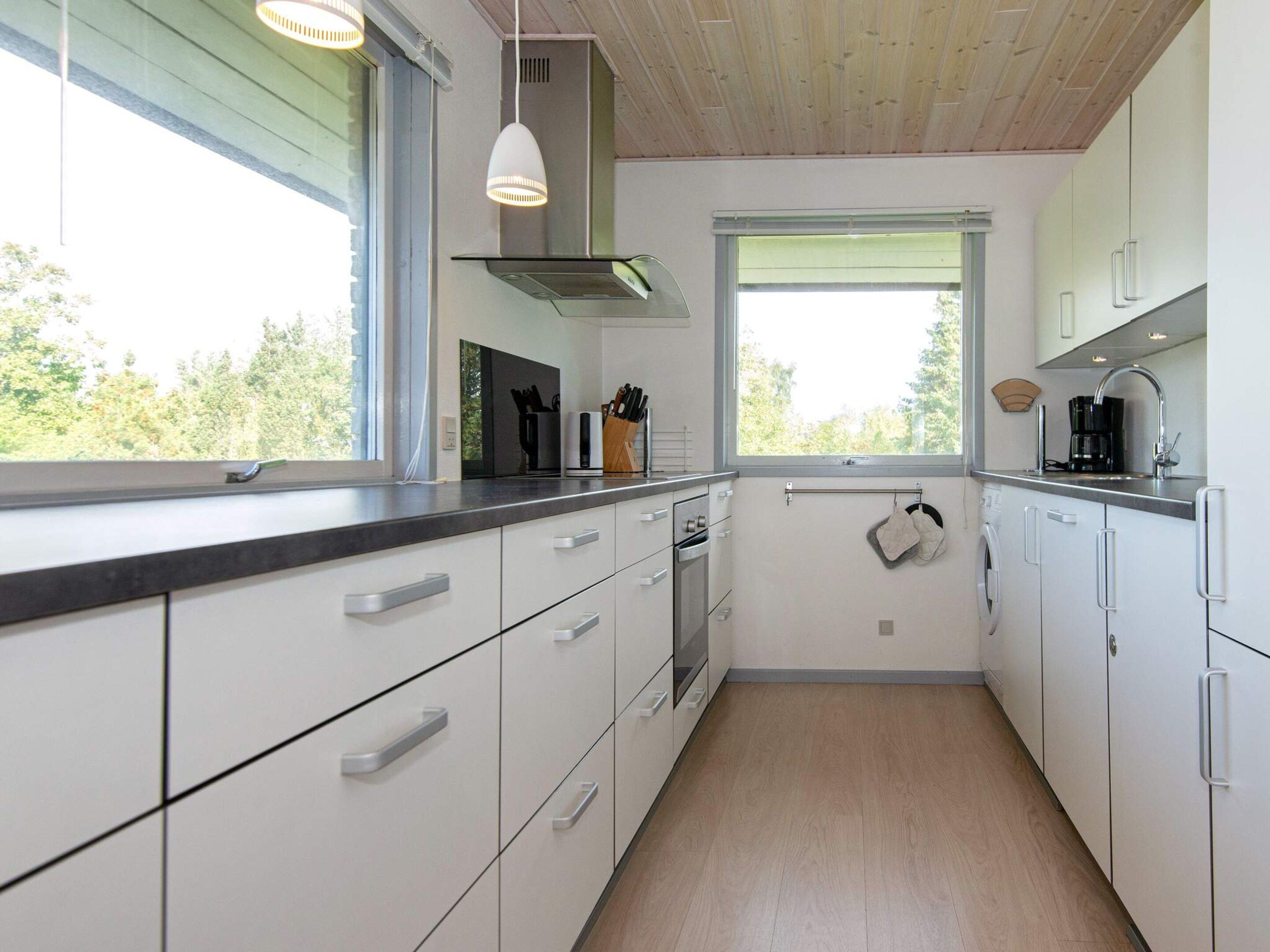 A modern kitchen with white cabinetry, a stainless steel range hood, and a window providing natural light.