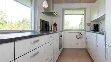 A modern kitchen with white cabinetry, a stainless steel range hood, and a window providing natural light.