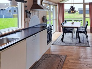 A kitchen with a large window, a dining area with a table and chairs, and a view of a grassy field.