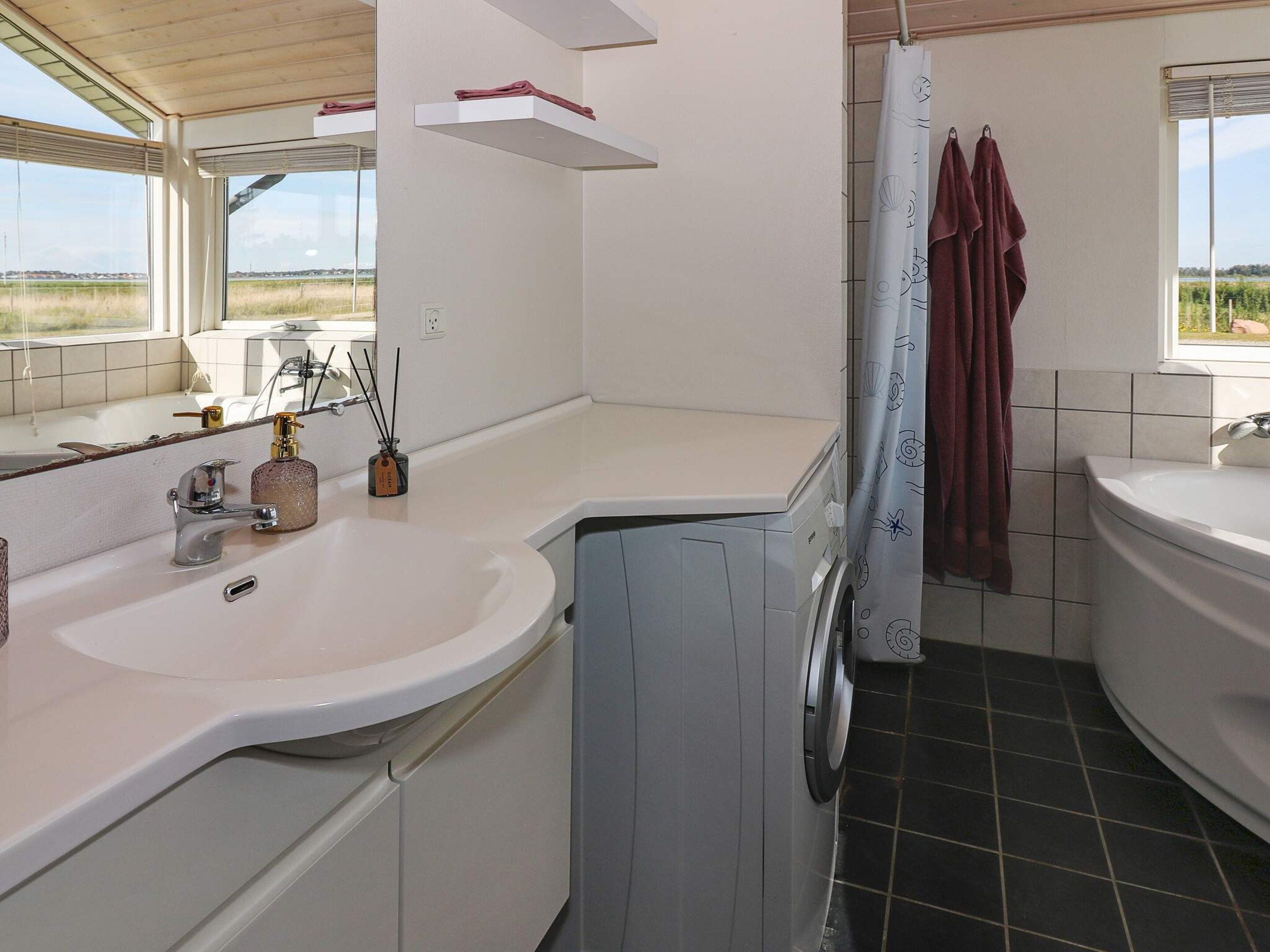 A bathroom with a white sink, a mirror, a washing machine, and a shower curtain.