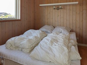 A room with a wooden paneled wall, a bed with white bedding, and a window with a view of a house. - Spacious Holiday Home in Storvorde near Sea (Storvorde)