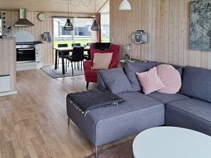 A modern living room with a grey sofa, red chair, and a dining area with a table and chairs. - Spacious Holiday Home in Storvorde near Sea (Storvorde)