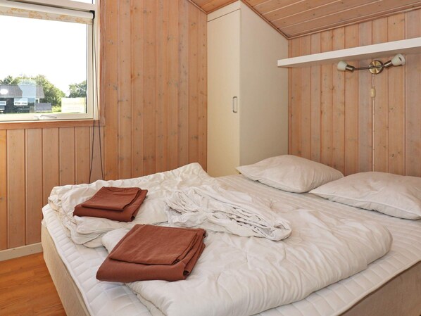 A bedroom with a bed, a wooden wall, a window, and a bedside table.