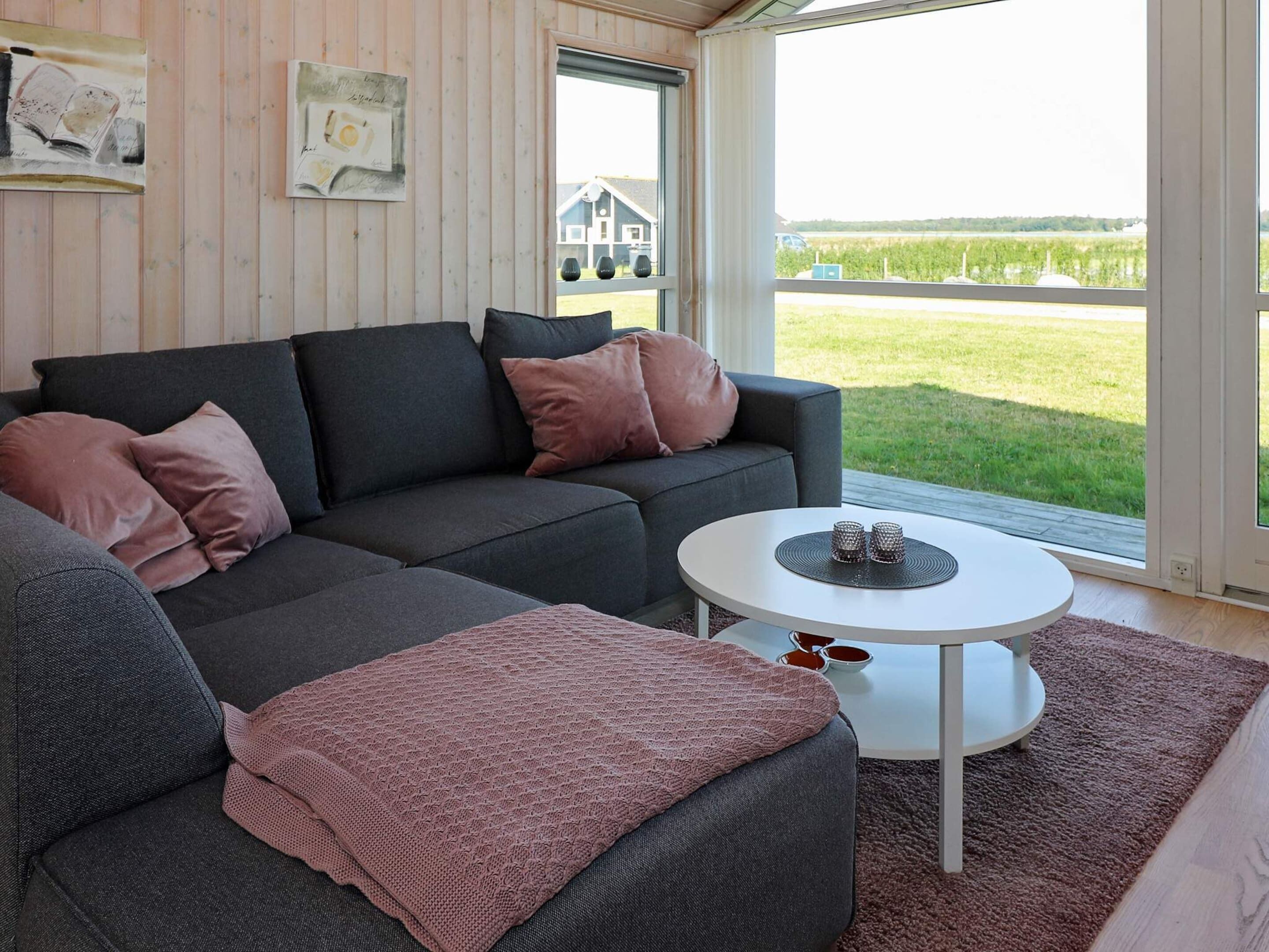 A modern living room with a grey sectional sofa, a round white coffee table, and a view of a green field through a large window.
