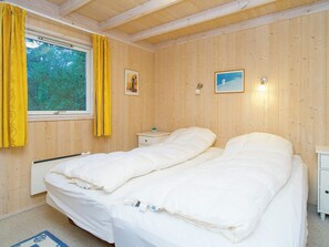 Une pièce aux murs en bois, un lit avec une literie blanche, une table de chevet, une fenêtre avec des rideaux et deux lampes fixées au mur.
