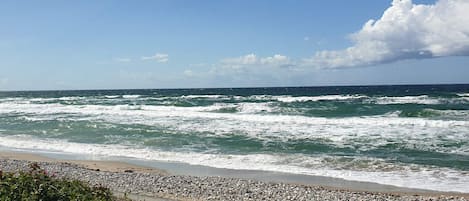 A beach with waves, a pebbly shore, and a clear sky.