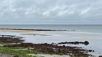 A coastal landscape with a rocky shoreline, a sandy beach, and a calm sea under a cloudy sky.