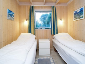 A room with two single beds, a small white chest of drawers, a window with curtains, and a painting on the wall. - 5 Star Holiday Home in Graested (Graested)