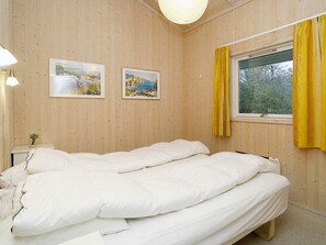 A bedroom with a bed, two framed pictures on the wall, a bedside table with a lamp, and a window with yellow curtains. - 5 Star Holiday Home in Graested (Graested)