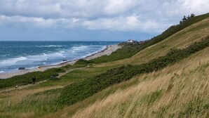 Un paisaje costero con playa, colinas cubiertas de hierba y una vista distante del océano.
