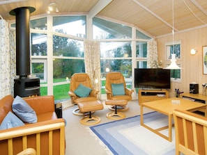 A cozy living room with a fireplace, two leather armchairs, a sofa, a TV, and large windows offering a view of the outdoors. - 5 Star Holiday Home in Graested (Graested)