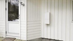 Pared exterior blanca con una puerta, una ventana y una caja eléctrica fijada a la pared.