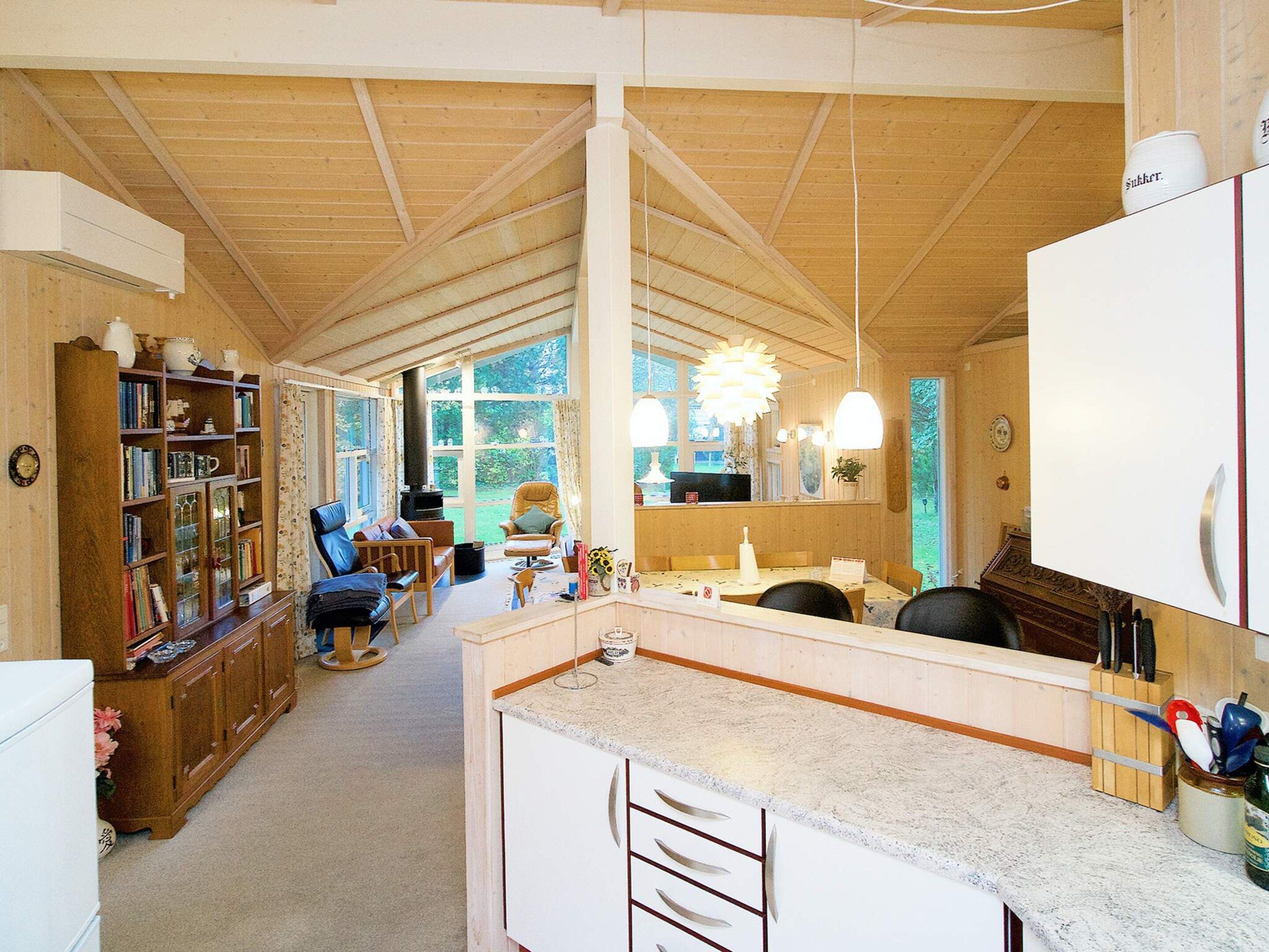 A spacious room with a wooden ceiling, a kitchen area with a marble countertop, and a seating area with a chair and a table.