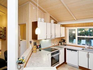 A modern kitchen with wooden cabinets, a built-in oven, a dishwasher, and a window with a view of greenery. - 5 Star Holiday Home in Graested (Graested)