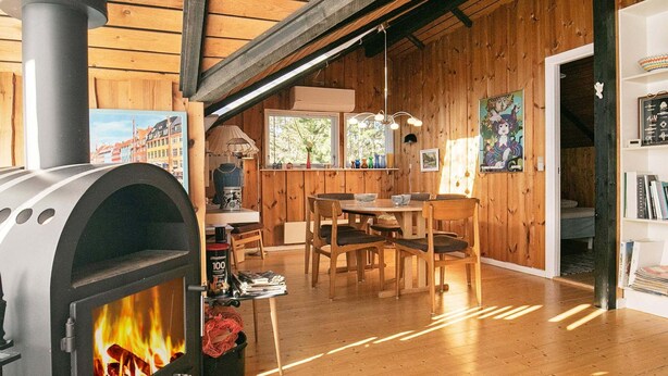 A rustic wooden interior with a wood stove, wooden dining table, chairs, and a bookshelf. - 6 Person Holiday Home in Saltum (Saltum)