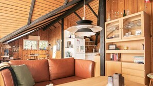 A cozy living room with a leather sofa, wooden shelves, and a dining table with a vase of flowers. - 6 Person Holiday Home in Saltum (Saltum)