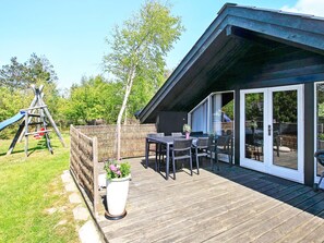 A wooden deck with a table and chairs, a swing set, and a fenced garden area. - 6 Person Holiday Home in Saltum (Saltum)