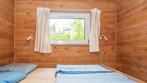 Una camera in una baita di legno con un letto, una finestra con tende e vista sul verde circostante.