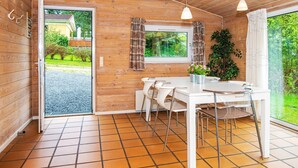 Interno di una baita in legno con zona pranzo, ampie finestre e vista sul verde circostante.