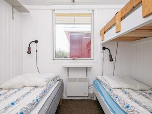 A dormitory room with bunk beds, a window with a red curtain, and a wall-mounted heater.
