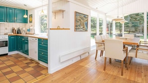Een moderne keuken met blauwgroene kastjes, een houten eettafel en een groot raam met uitzicht op groen.