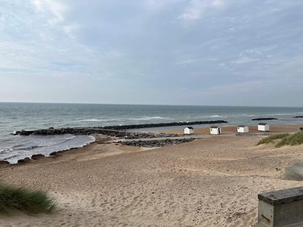 A beach with a rocky breakwater and several small white structures, likely beach huts, on the sand.