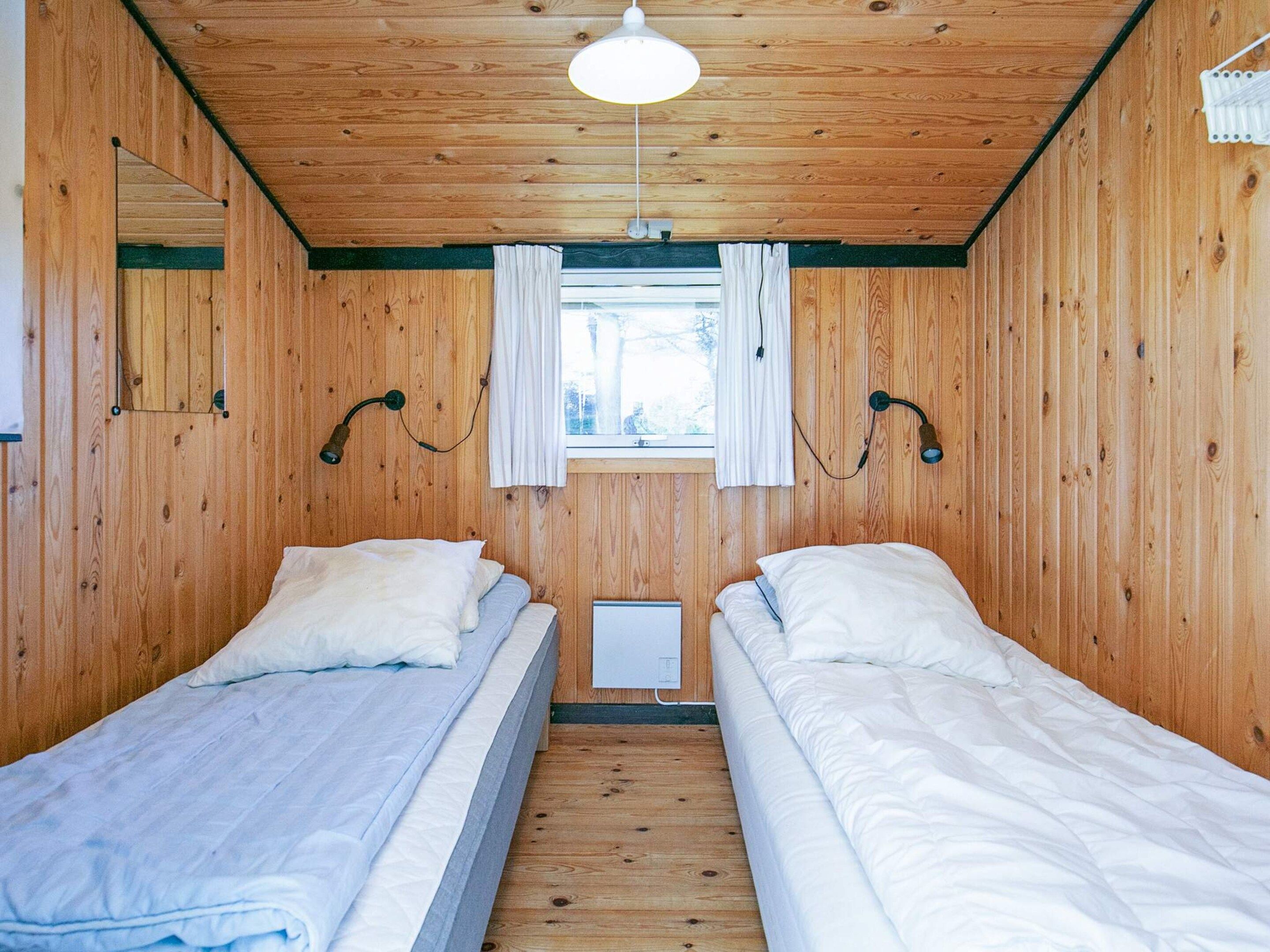Una habitación con dos camas, paredes de madera, una ventana con cortinas y una lámpara en el techo.