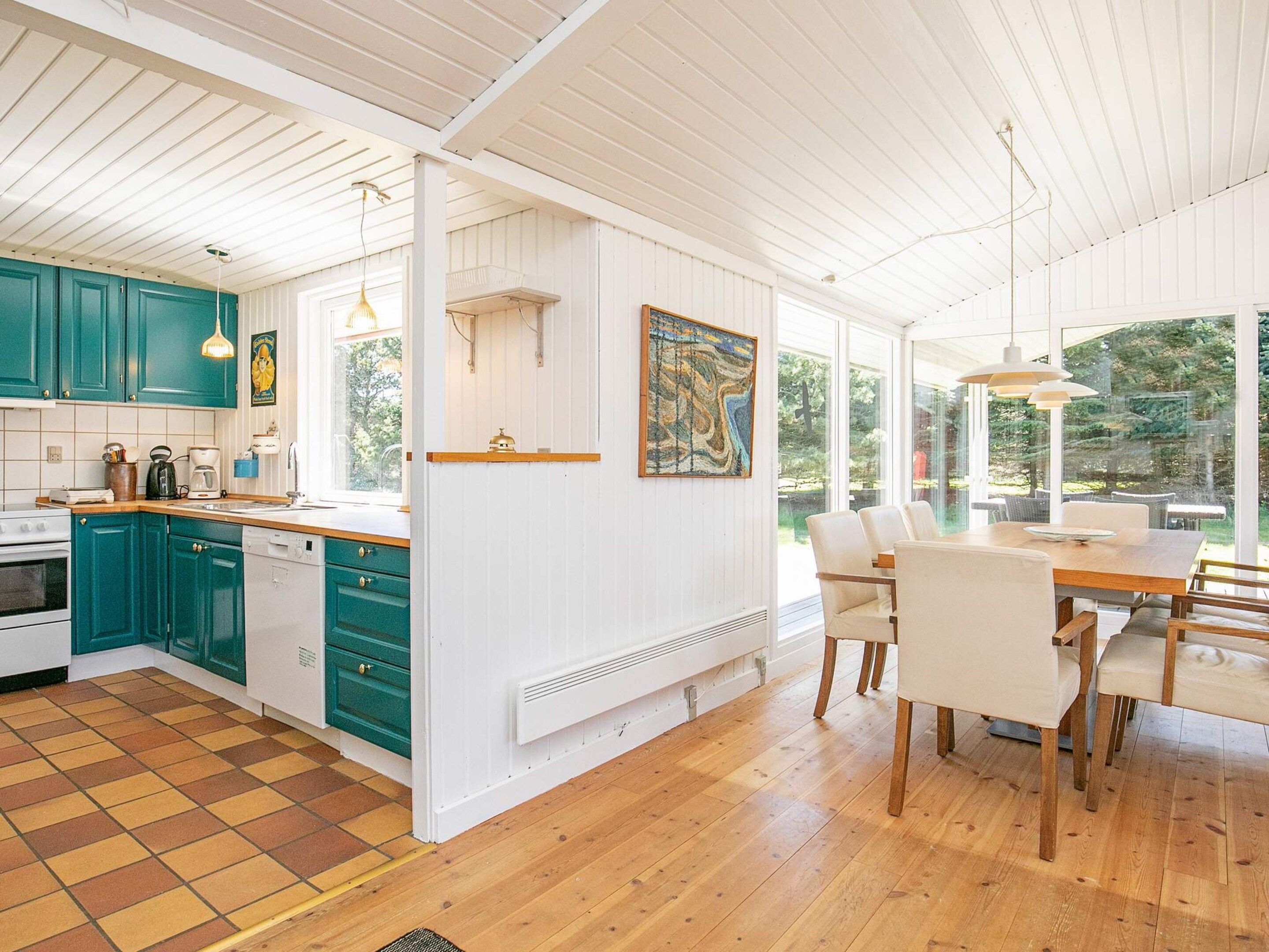 Una cocina moderna con armarios color turquesa, un comedor con mesa y sillas de madera, y ventanas amplias con vistas al verdor.