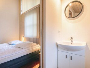 Une chambre à coucher comprenant un lit, une table de chevet, un miroir rond et un lavabo blanc avec un meuble sous-vasque.