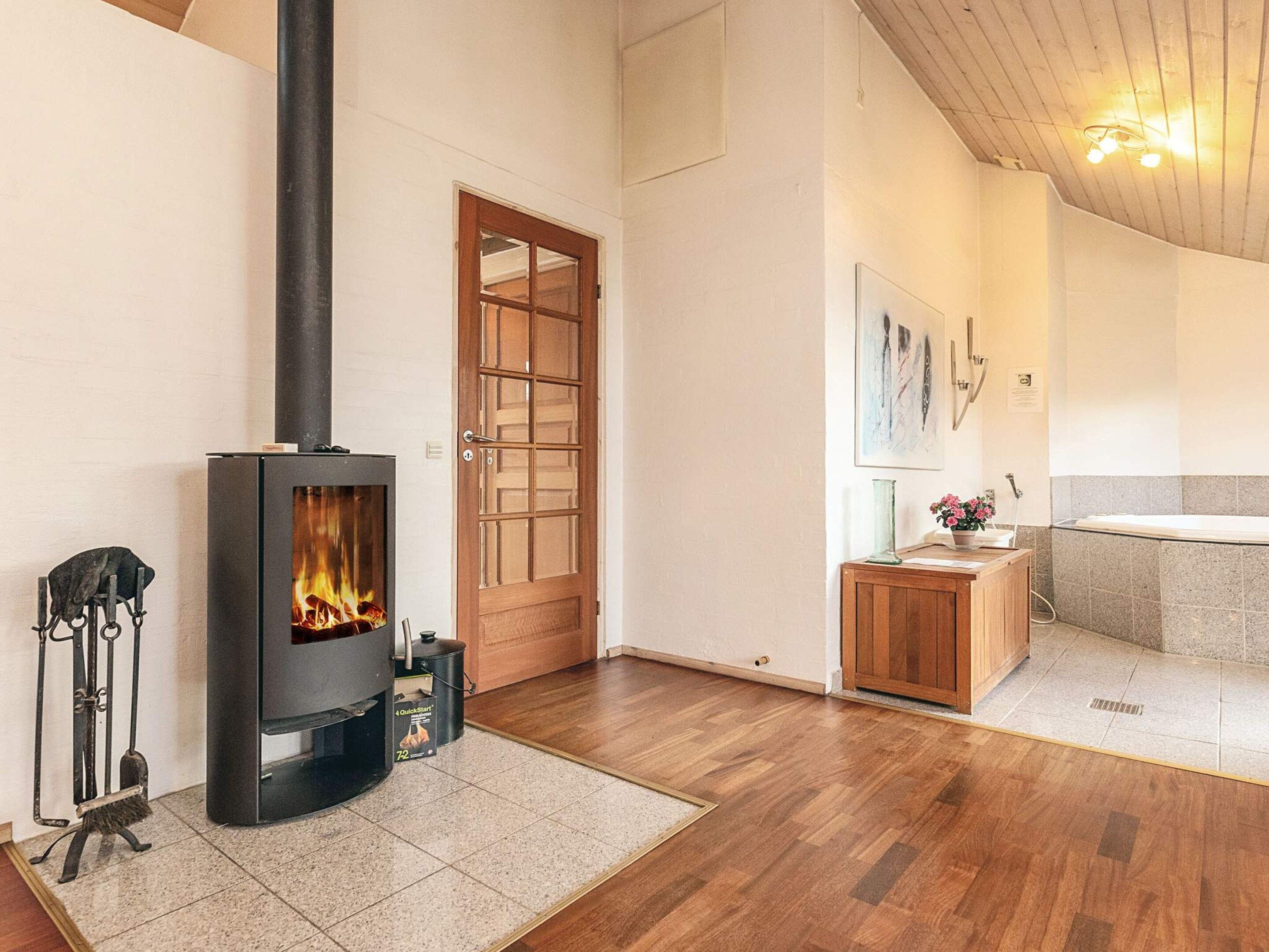 A room with a wood-burning stove, a wooden door, a small cabinet, and a tiled floor.