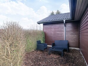 Un espace patio avec deux chaises et une table, entouré d’une clôture en bois et d’une haie.