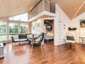 Un vaste espace de vie avec une chambre en mezzanine, de grandes fenêtres et un plafond en bois.