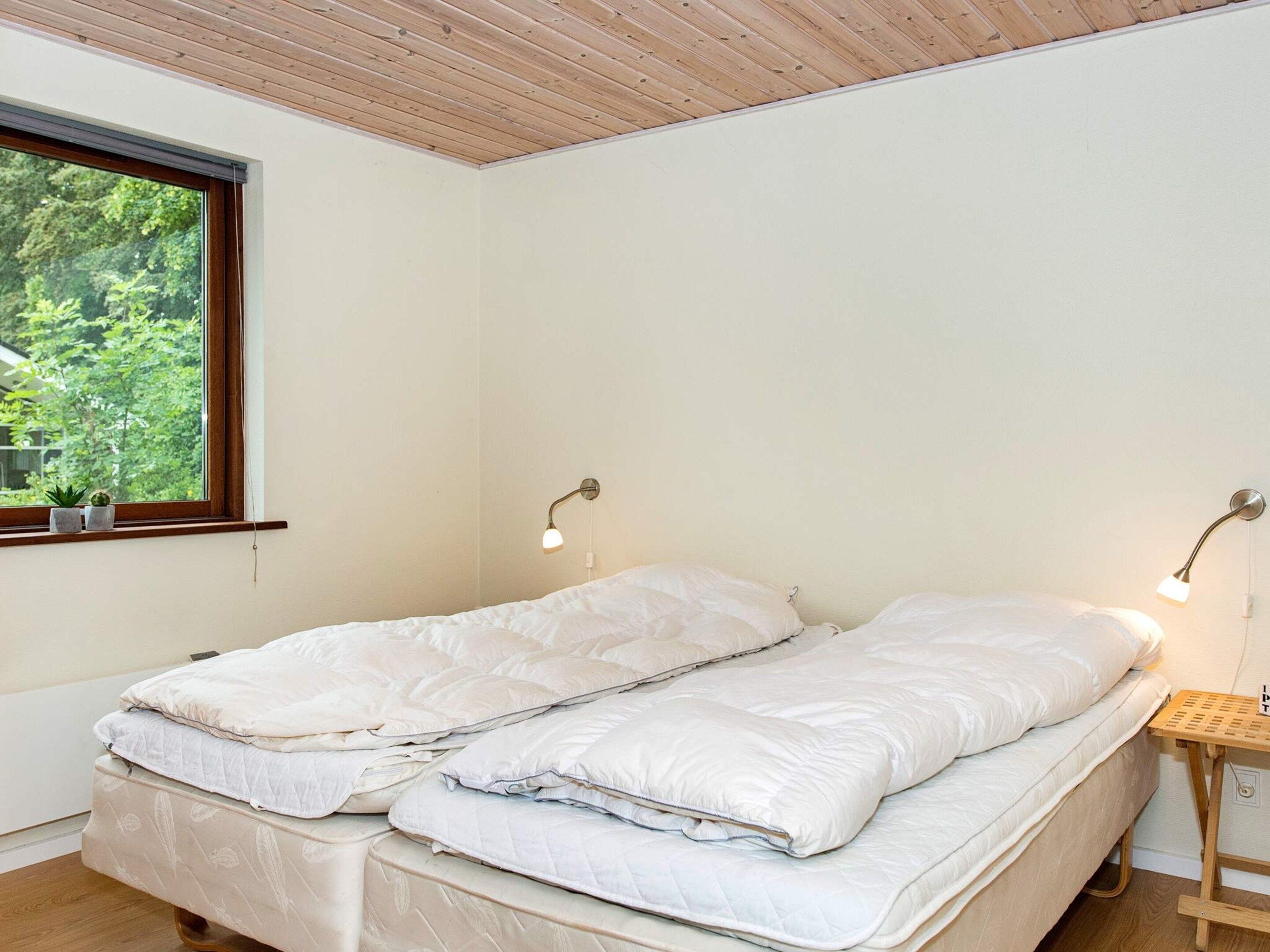 A room with a bed, two bedside lamps, a window with a view of greenery, and a small wooden table.