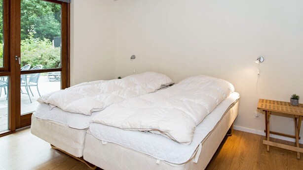 A bedroom with a double bed, a wooden ceiling, and a view of the outdoors through a glass door. - 4 Star Holiday Home in Aabenraa (Aabenraa)