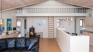 A loft-style living space with a wooden ceiling, a black leather sofa, a kitchen area, and a fireplace. - 4 Star Holiday Home in Aabenraa (Aabenraa)