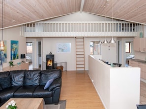 Un ambiente abitativo in stile loft con soffitto in legno, un divano in pelle nera, una zona cucina e un caminetto.