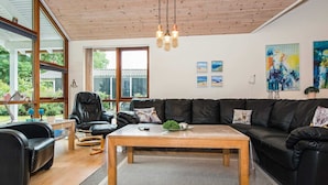 A modern living room with a wooden ceiling, leather sofas, a coffee table, and large windows offering a view of greenery. - 4 Star Holiday Home in Aabenraa (Aabenraa)